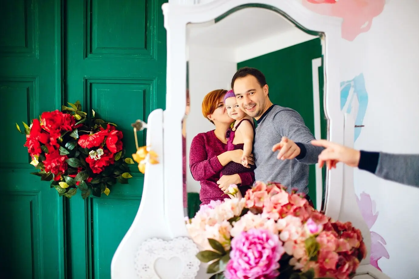 Отражение счастливых родителей с маленькой девочкой в белом зеркале.